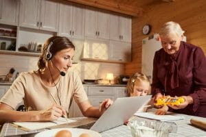 Woman writing before laptop while granny playing with kid planning permission