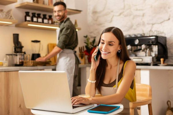 Wife receiving calls from clients while sitting at the laptop and having family business